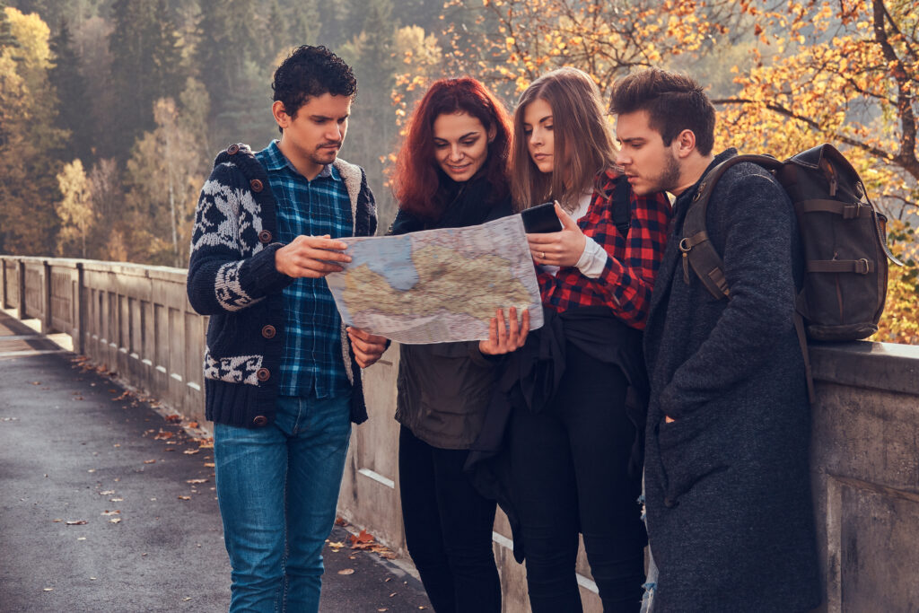 photo of young friends looking at map and planning trip at autumn forest.